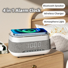 4-in-1 alarm clock with a wireless charger and speaker on a nightstand. The alarm clock is black and has a digital display. The wireless charger is white and is located on the top of the alarm clock. The speaker is black and is located on the side of the alarm clock. The nightstand is made of wood and has a lamp on it